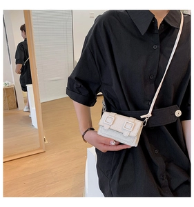 Détail du mini sac blanc à texture tissée porté sur une chemise noire élégante
