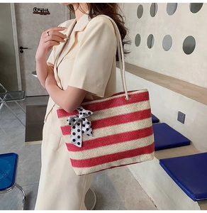 Detail of red and white striped straw tote bag featuring a large polka dot bow charm