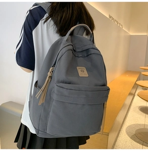 Detail view of a gray nylon backpack with a large zipper pocket and a leather brand label