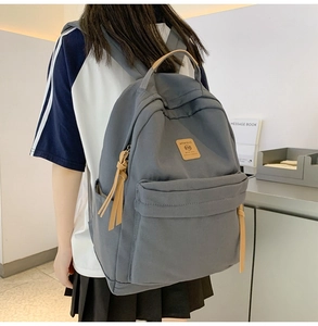 Detail of grey nylon backpack featuring leather zipper pulls and front logo patch