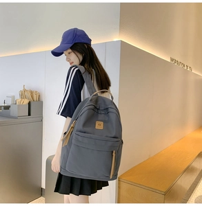 Detail view of a gray canvas backpack with brown leather patch and side pocket storage