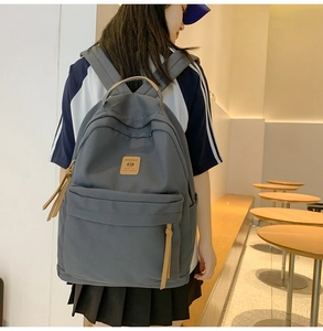Close-up of gray nylon backpack with brown leather handle and brand patch in a cafe setting