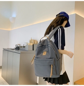 Detail of grey-blue nylon backpack showing the front leather logo and zipper with long tassel