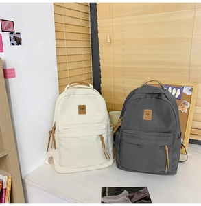 Minimalist canvas backpacks in white and dark grey with leather logo patch and puller