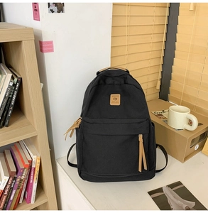 Detail of minimalist black nylon backpack with brown leather logo and side water bottle pocket