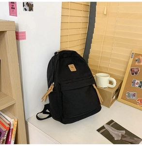 Detail of black canvas backpack with vintage brown leather zipper pulls and logo patch