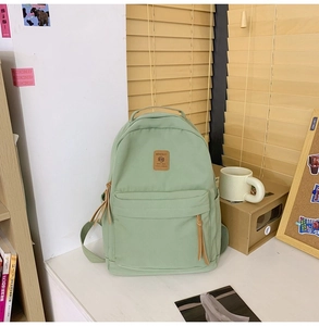 Detail view of mint green nylon backpack with front pocket and brown leather logo patch