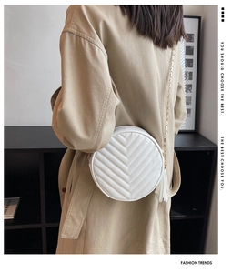 Close-up of white round quilted crossbody bag with golden chain and tassel detail