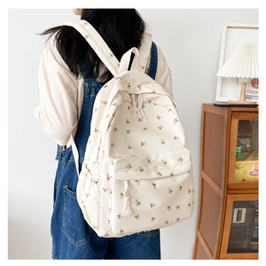 Side view of cream-colored backpack with pink rose floral print and cotton tassels