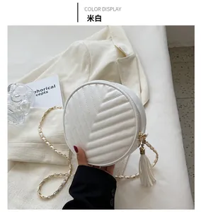 Detail of off-white quilted round crossbody bag with metal chain strap and tassel charm