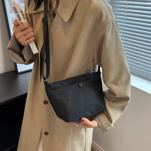 Minimalist black nylon shoulder bag for women shown with stylish urban trench coat outfit