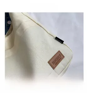 Close-up of the beige canvas fabric texture with a brown leather logo patch and stitching