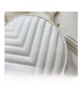Detail shot of white round quilted shoulder bag with V-shaped stitching and tassel