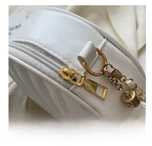 Detailed close-up of smooth gold zipper and tassel pendant on the white crossbody bag