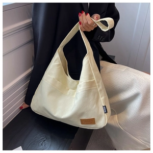 Detail shot of a beige canvas tote bag showing the wide strap and brown leather patch