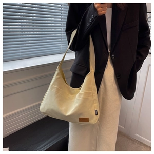 Detail of a cream canvas tote bag featuring a brown SPORT patch and wide shoulder strap