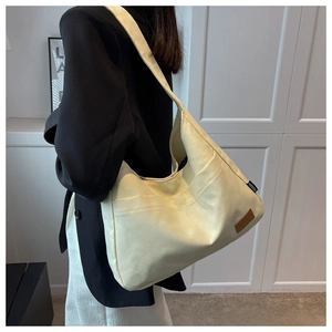 Detail of cream canvas tote bag with large front pockets and brown leather logo patch