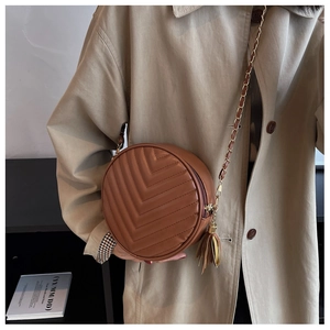 Detail of a brown quilted round crossbody bag featuring a leather chain strap and fringe tassel