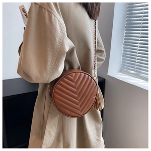 Detailed view of brown circular crossbody bag with V-shaped quilting and leather tassel