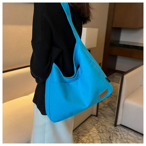 Detail of bright blue canvas tote bag with brown leather SPORT patch in indoor setting