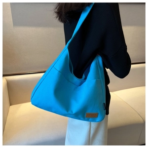 Blue canvas tote bag with outer pocket and brown leather patch shown on model shoulder