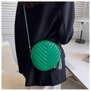 Detail of green round quilted crossbody bag with stylish long tassel and metal chain strap