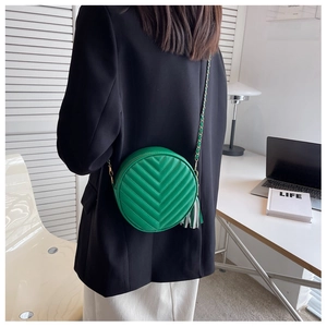 Detail of round green crossbody bag with V-quilting, tassel and chain strap on model