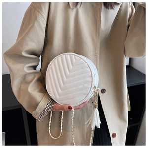Detail of white round quilted crossbody bag with gold chain and leather tassel charm
