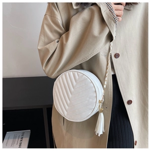 Detail of white round crossbody bag featuring chevron quilting and white tassel charm strap