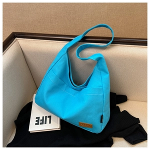 Detail of a bright blue canvas tote bag with a brown leather tag on a stylish sofa
