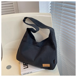 Detail of black canvas tote bag with front pocket and sport leather label on a chair