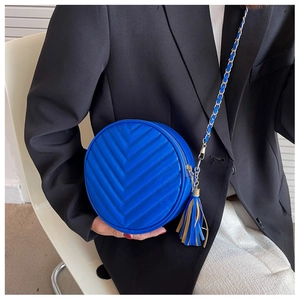 Close-up of royal blue round crossbody bag with chevron quilting and dual-tone tassel detail