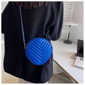 Detail of bright blue round crossbody bag with chevron quilting and golden chain strap