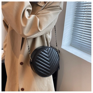 Detail of black round crossbody bag with V-shaped quilting and chain strap on a model