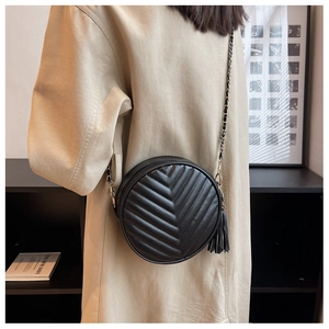 Detail of black round crossbody bag featuring V-shaped quilting and tassel fringe