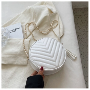 Detail of white round quilted crossbody bag with tassel and chain strap on textured blazer