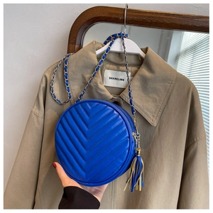 Detail of blue quilted round crossbody bag with metal chain strap and fringe tassel