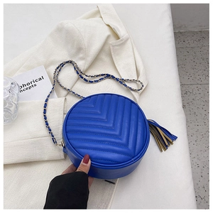 Detailed close-up of blue quilted round crossbody bag with chain strap and fringe tassel