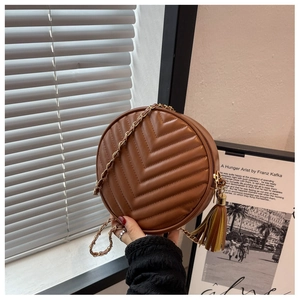 Close-up of brown round quilted crossbody bag with gold chain strap and leather tassel