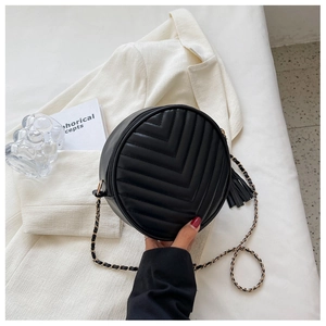 Detailed view of quilted black round bag with V-shaped texture and leather fringe tassel