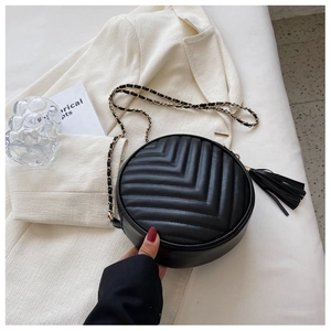 Macro shot of black quilted round bag with stylish tassel and golden chain strap