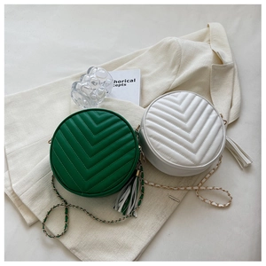 Detail of round quilted crossbody bags in green and cream with tassel and chain strap