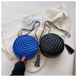Detail of round V-quilted crossbody bags in blue and black with gold chain and tassels