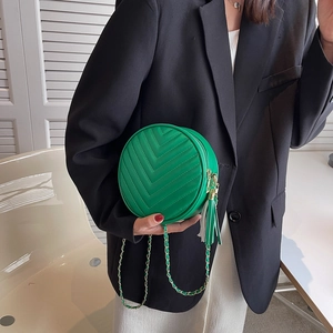 Green round crossbody bag with V-shaped quilting and gold chain strap worn by a model