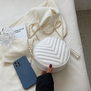 White round crossbody bag with V-quilted faux leather, gold chain strap and tassel