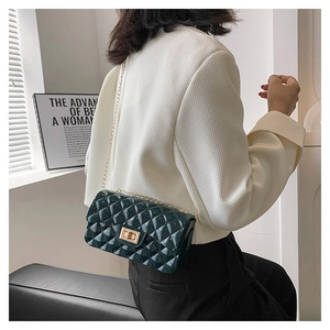 Detail of dark green quilted crossbody bag with glossy finish and gold chain strap