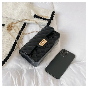 Close-up of quilted black chain bag with gold metal lock on a white fabric background