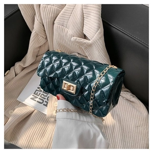 Detail of green quilted bag with glossy finish and gold metal chain strap on fabric