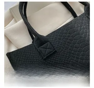 Macro detail of reinforced X-shaped stitching and crocodile texture on black tote bag
