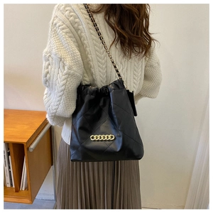 Fashionable black quilted shoulder bag with gold chain strap on a model in a library